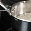 A close-up shot of a deBuyer Affinity Stielkasserolle (saucepan) with water boiling inside, placed on a black stovetop. Voir les images du produit