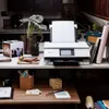 A white Canon PIXMA TS8751 WLAN color multifunction photo printer is shown on a desk with various office supplies and decorative items. Podgląd zdjęcia produktu