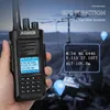 A hand holding a walkie-talkie with GPS functionality displayed on its screen, with a background suggesting outdoor use and communication equipment. Produktbild-Vorschau