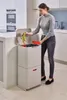 A woman is throwing away banana peels into a multi-compartment trash can in a modern kitchen. Podgląd zdjęcia produktu