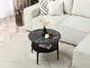 A round coffee table with a marble top and a lower shelf is placed on a rug in front of a sectional sofa. Produktbild-Vorschau