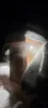A wooden smoking chamber covered in snow at night, with steam rising from it and a light illuminating the scene. Náhled obrázku produktu