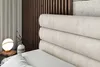 A close-up view of a bed with a plush headboard and a bedside table with a lamp and vase. Produktbild-Vorschau