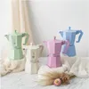 Four colorful Bialetti Moka pots are arranged on a marble surface with draped fabric and dried flowers. Anteprima dell’immagine prodotto
