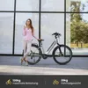 A woman stands next to an e-bike, holding a cup. Produktbild-Vorschau