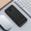 A black phone case with a carbon fiber look is placed on a light gray surface next to a white computer mouse and a portion of a keyboard. Produktbild-Vorschau