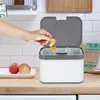 A hand is shown dropping an orange peel into a white and gray compost bin in a kitchen setting. Produktbild-Vorschau