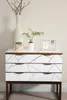 A white dresser with geometric patterns on the drawers, decorated with a vase of branches, a potted plant, and a wire photo frame. Podgląd zdjęcia produktu