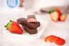 Chocolate-covered strawberry protein bars on a white plate with fresh strawberries. Produktbild-Vorschau