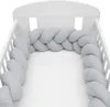 A close-up view of a braided crib bumper in a light gray color, placed inside a white crib. Náhľad obrázku produktu