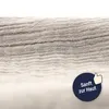 Close-up of a textured fabric, likely muslin, with a circular overlay containing a thumbs-up icon and German text. Produktbild-Vorschau