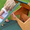 A young girl is looking into a wooden pet house with a green roof. Produktbild-Vorschau