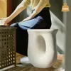 A person sits next to a white speckled stool, with a table on the left. Náhled obrázku produktu