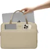 A hand is placing a laptop into a beige laptop bag. The bag has pockets on the front holding a phone and a card. Náhľad obrázku produktu