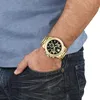 A person's arm wearing a gold watch and blue shirt, with their hand in their jeans pocket. Anteprima dell’immagine prodotto