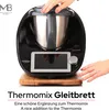 A black Thermomix appliance is shown on a wooden board, with hands interacting with it. Produktbild-Vorschau