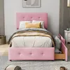 A pink upholstered bed with a tufted headboard and storage drawers, set up in a bedroom. Náhled obrázku produktu