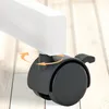 Close-up of a black caster wheel with a brake lever attached to a white furniture leg, with orange arrows indicating rotation. Anteprima dell’immagine prodotto