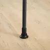 A close-up view of the bottom of a black metal pole with an adjustable black plastic foot on a light wood-grain floor. Podgląd zdjęcia produktu