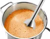 A close-up of an immersion blender in a pot of orange liquid. Produktbild-Vorschau