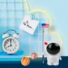 A desk setup with an alarm clock, a pencil sharpener shaped like an astronaut, and decorative spheres against a tiled blue background. Anteprima dell’immagine prodotto