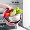 A hand holding a pink colander with vegetables and water draining out. Produktbild-Vorschau