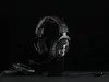 A black Logitech G PRO X gaming headset is displayed on a black stand against a black background. Two extra ear pads are placed in the foreground. Náhled obrázku produktu