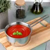 A stainless steel saucepan filled with tomato sauce and garnished with a basil leaf, placed on a wooden cutting board. In the background, there is a jar of herbs and a bottle of olive oil. Produktbild-Vorschau