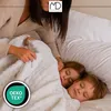 A woman tucks two sleeping children into a white blanket on a bed. Náhled obrázku produktu