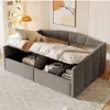 A grey upholstered daybed with storage compartments open, revealing folded blankets and linens inside. The daybed is set up in a room with a patterned rug and a framed artwork on the wall. Produktbild-Vorschau