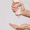 A hand squeezes a pink tube of hair product, dispensing a white liquid into another hand. Náhled obrázku produktu