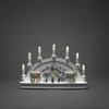 A white LED wooden silhouette of houses and a church with candle-shaped lights, set against a plain gray background. Produktbild-Vorschau