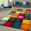 A colorful geometric rug is laid out on a wooden floor in a living room setting, with a sofa and chair in the background. Produktbild-Vorschau