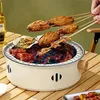A portable charcoal grill with food cooking on it, placed on a wooden table with a bottle of beer. Anteprima dell’immagine prodotto