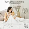 A woman is reading a book in bed, covered by a white blanket, with a fan and a vase of flowers in the background. Anteprima dell’immagine prodotto