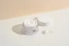 A jar of Anua Heartleaf 70% Intense Calming Cream is shown on a white surface with a light beige background. The lid is off, and a small amount of cream is scooped out onto a spatula. Produktbild-Vorschau
