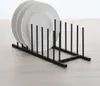 A black metal plate rack holding three white plates, placed on a light-colored wooden surface. Produktbild-Vorschau