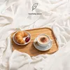 A cozy breakfast scene with a croissant, jam, and coffee on a tray, set against a soft, white blanket. Voir les images du produit