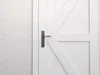 A close-up view of a white wooden door with a dark metal handle. Produktbild-Vorschau