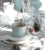 A table setting with a pale blue latte cup, plates, napkins, glasses, and pinecones, suggesting a festive or winter theme. Voir les images du produit