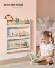A young girl sits on the floor reading a book next to a white children's bookshelf filled with books and stuffed animals. Produktbild-Vorschau