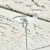 A close-up view of a white ceiling clip with a metal hook attached, mounted on a textured white ceiling. Produktbild-Vorschau