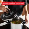 A person is holding the lid of a pressure cooker, showing its features. Voir les images du produit