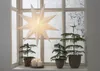 A paper star lantern hangs in a window with frosted glass, and three small Christmas trees in pots are on the windowsill, along with three white candles. Podgląd zdjęcia produktu