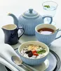 A table setting with a teapot, creamer, teacup, and a bowl of yogurt with fruit. Anteprima dell’immagine prodotto