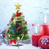 A miniature Christmas tree decorated with ornaments, bows, and a star topper, set against a snowy background with lit red candles and a decorative ornament. Náhled obrázku produktu