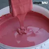 A close-up view of pink liquid being poured from a spatula into a white bucket. Produktbild-Vorschau