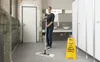 A woman is mopping a floor in a public restroom, with a wet floor sign nearby. Podgląd zdjęcia produktu