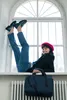 A woman is sitting on a windowsill with her legs up, wearing jeans, a blazer, a beret, and loafers. A bag is placed on a radiator below. Voir les images du produit