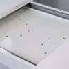 A close-up view of the interior of a white, high-gloss drawer or cabinet, showing metal drawer slides and several small screws. The surface appears clean and reflective. Produktbild-Vorschau